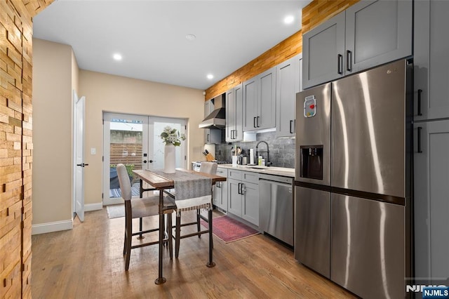 kitchen featuring stainless steel appliances, light countertops, backsplash, wall chimney range hood, and wood finished floors