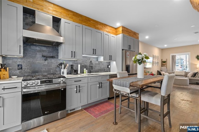 kitchen featuring light countertops, appliances with stainless steel finishes, light wood-style floors, a sink, and wall chimney exhaust hood