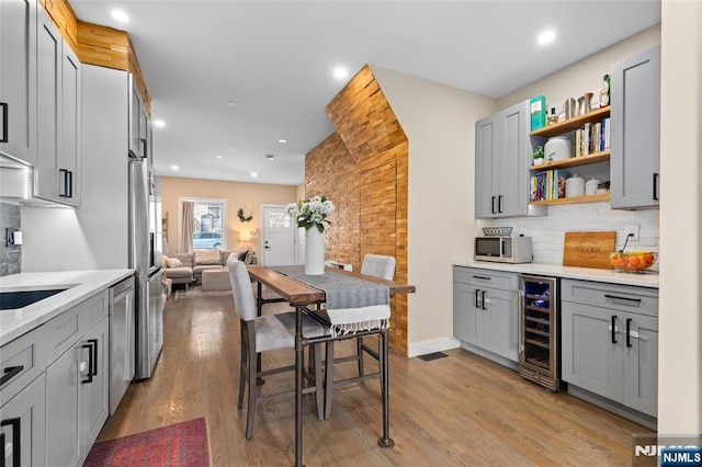 kitchen with stainless steel appliances, wine cooler, light wood-type flooring, and gray cabinetry