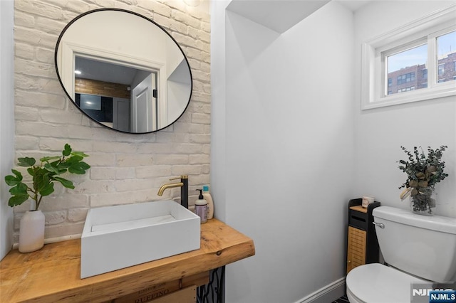 half bath with brick wall, a sink, and toilet