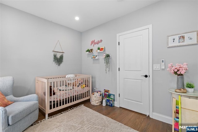 bedroom featuring a nursery area, baseboards, wood finished floors, and recessed lighting