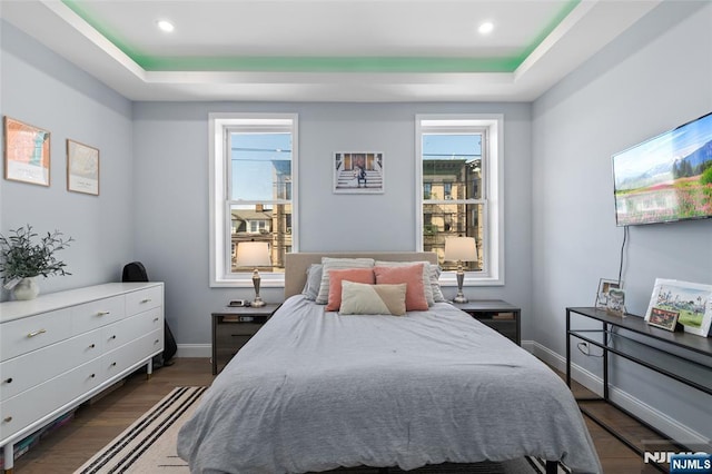 bedroom featuring dark wood-style floors, baseboards, a raised ceiling, and recessed lighting