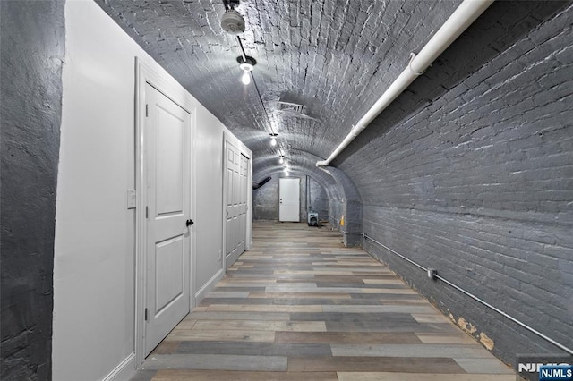 hallway with brick ceiling, vaulted ceiling, wood finished floors, and visible vents