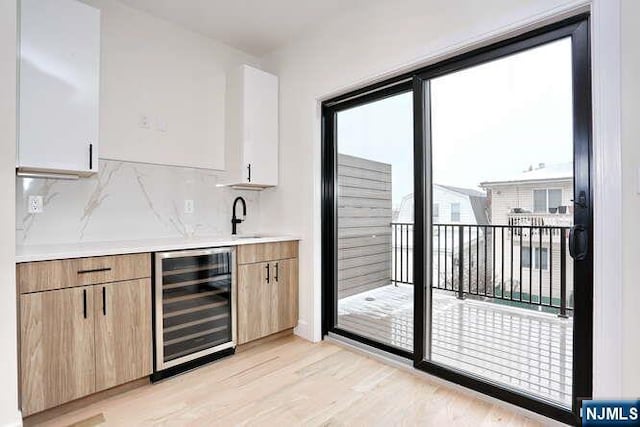 bar featuring beverage cooler, backsplash, a sink, and light wood-style flooring