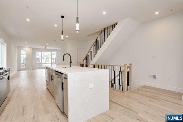 kitchen with light wood-style floors, appliances with stainless steel finishes, open floor plan, and a sink