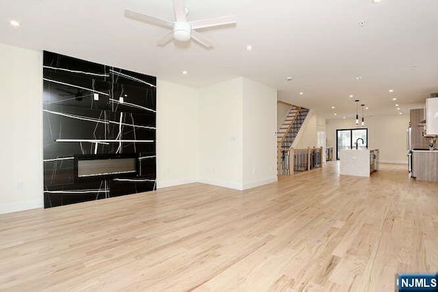 unfurnished living room featuring stairs, light wood finished floors, baseboards, and recessed lighting