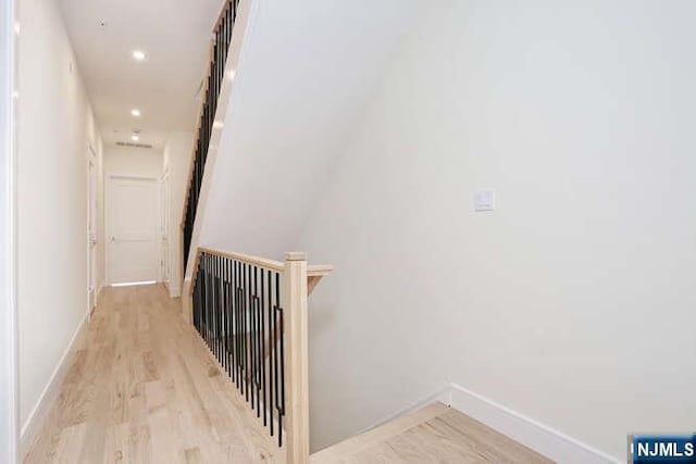 hallway with light wood-type flooring, an upstairs landing, baseboards, and recessed lighting