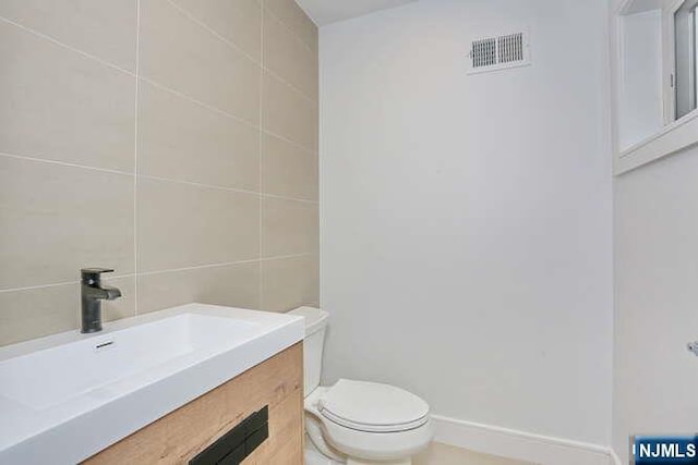 bathroom featuring baseboards, visible vents, toilet, vanity, and tile walls