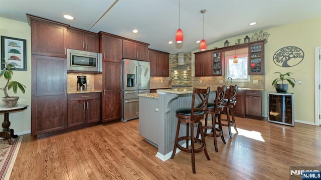 kitchen with stainless steel appliances, wine cooler, a kitchen breakfast bar, wall chimney exhaust hood, and light wood-type flooring