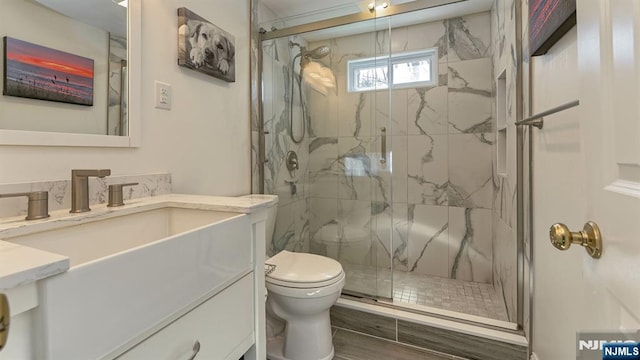 full bathroom with a marble finish shower, toilet, and vanity