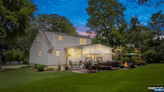 back of property featuring a patio area, a hot tub, a shingled roof, and a yard