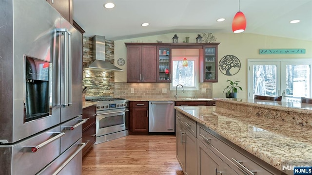 kitchen with light wood-style flooring, stainless steel appliances, decorative backsplash, vaulted ceiling, and wall chimney exhaust hood