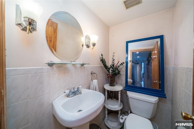 bathroom with a wainscoted wall, tile walls, visible vents, toilet, and a sink