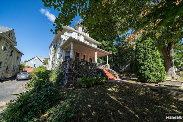 view of side of home featuring covered porch, stairs, and a chimney