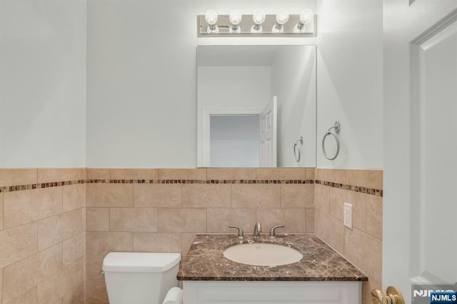 half bath with toilet, a wainscoted wall, tile walls, and vanity