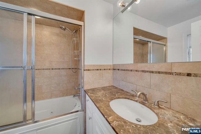 full bathroom with bath / shower combo with glass door, vanity, and tile walls