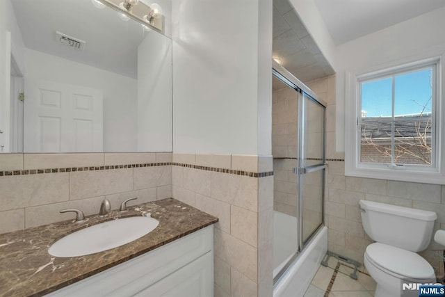 bathroom featuring tile walls, toilet, combined bath / shower with glass door, vanity, and tile patterned flooring