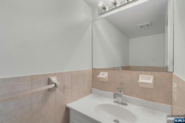 bathroom with a wainscoted wall, visible vents, tile walls, and vanity