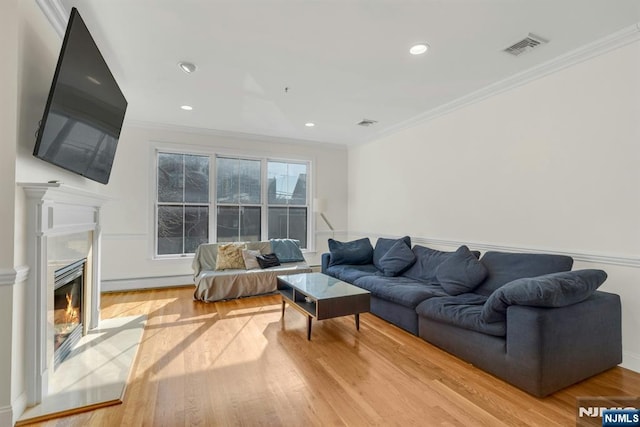 living area with light wood-style floors, visible vents, crown molding, and a premium fireplace