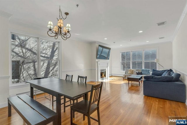 dining room with crown molding, light wood finished floors, visible vents, a fireplace with flush hearth, and a chandelier