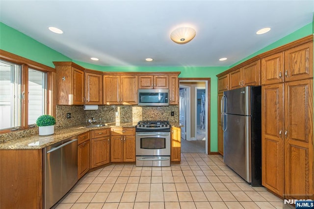 kitchen with tasteful backsplash, appliances with stainless steel finishes, brown cabinetry, and light tile patterned flooring