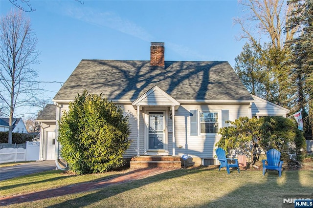 cape cod house with a shingled roof, fence, a chimney, and a front lawn