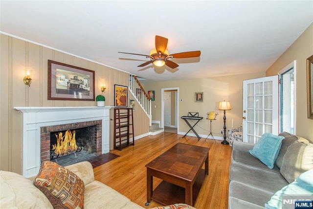 living room with baseboards, a ceiling fan, wood finished floors, stairs, and a fireplace