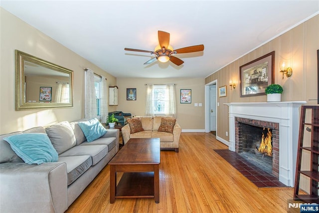 living area featuring a ceiling fan, a fireplace, light wood-style flooring, and baseboards