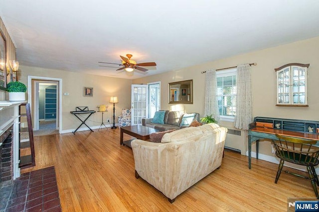 living room with baseboards, radiator heating unit, a brick fireplace, and light wood-style floors