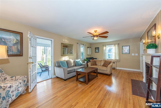 living room featuring light wood finished floors, a brick fireplace, a ceiling fan, and baseboards