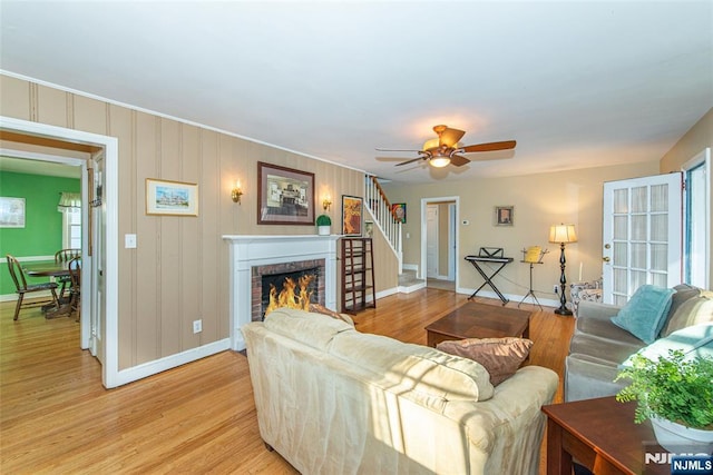 living room with a fireplace, light wood finished floors, a ceiling fan, baseboards, and stairs