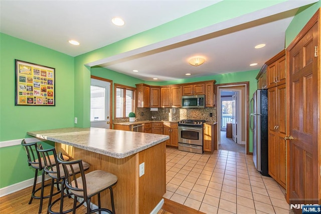 kitchen featuring stainless steel appliances, a breakfast bar, a peninsula, light countertops, and backsplash