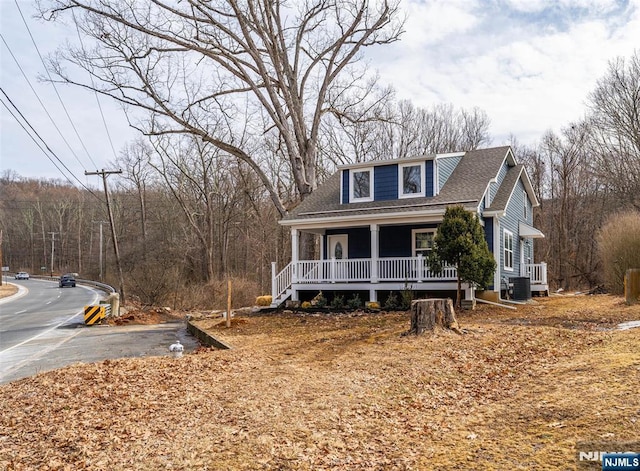 view of front of property featuring a porch, roof with shingles, central AC unit, and a view of trees