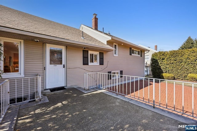 back of property featuring a patio, a shingled roof, a chimney, and fence