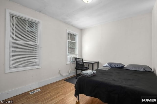 bedroom with cooling unit, visible vents, baseboards, and wood finished floors