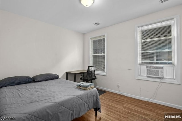 bedroom featuring cooling unit, baseboards, visible vents, and wood finished floors