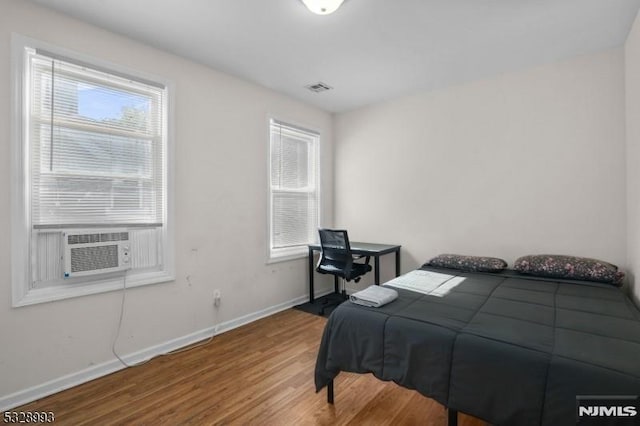 bedroom featuring multiple windows, wood finished floors, visible vents, and baseboards