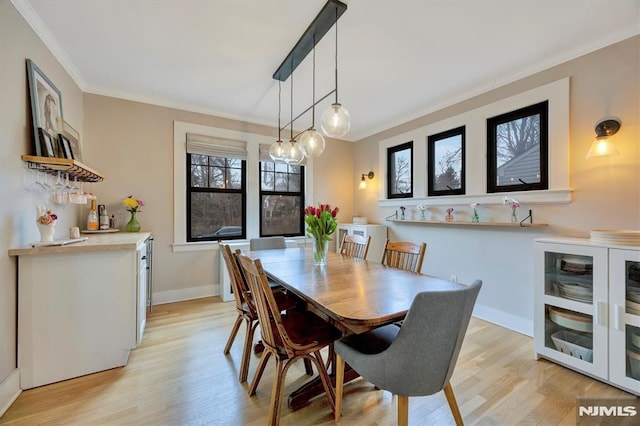 dining space featuring light wood-style floors, baseboards, and crown molding