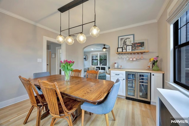 dining space with light wood-style flooring, wine cooler, arched walkways, and crown molding