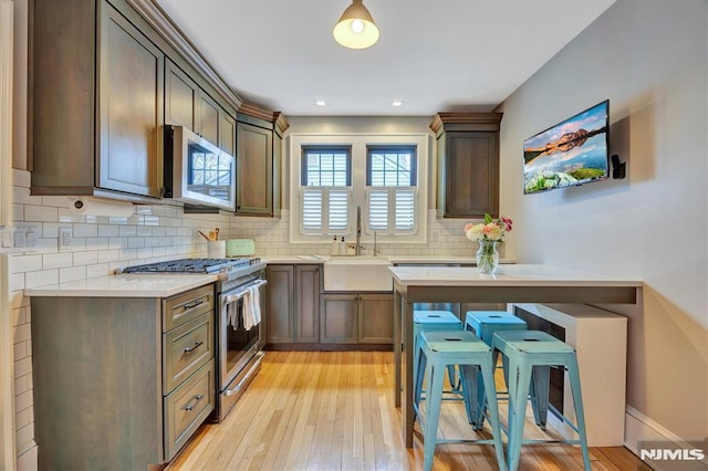 kitchen with stainless steel appliances, tasteful backsplash, light countertops, light wood-style floors, and a sink