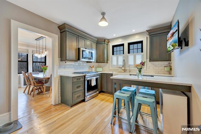 kitchen featuring light wood-type flooring, appliances with stainless steel finishes, light countertops, and backsplash