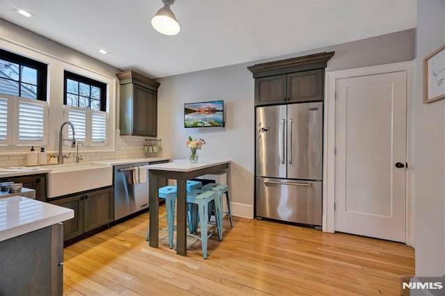 kitchen featuring light countertops, backsplash, appliances with stainless steel finishes, a sink, and light wood-type flooring