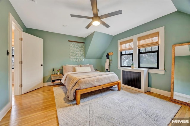 bedroom featuring light wood-style flooring, baseboards, vaulted ceiling, and a ceiling fan