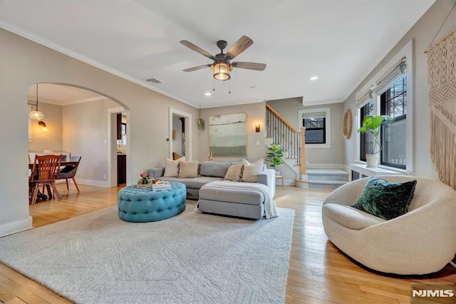 living area with arched walkways, visible vents, stairway, light wood-type flooring, and baseboards