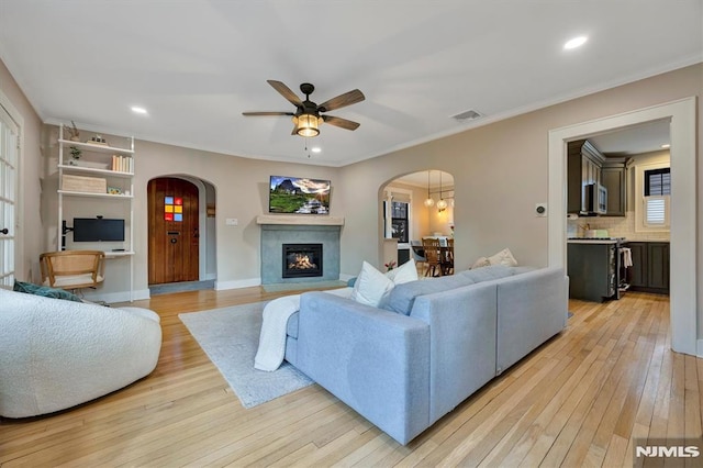 living area with visible vents, arched walkways, light wood-style flooring, and crown molding