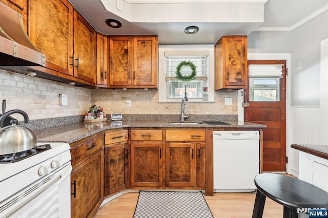 kitchen with white appliances, dark stone counters, brown cabinets, a sink, and exhaust hood