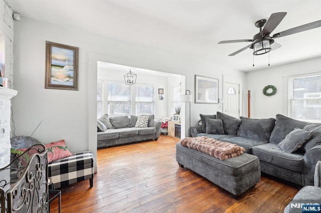 living area with ceiling fan with notable chandelier, plenty of natural light, and hardwood / wood-style flooring