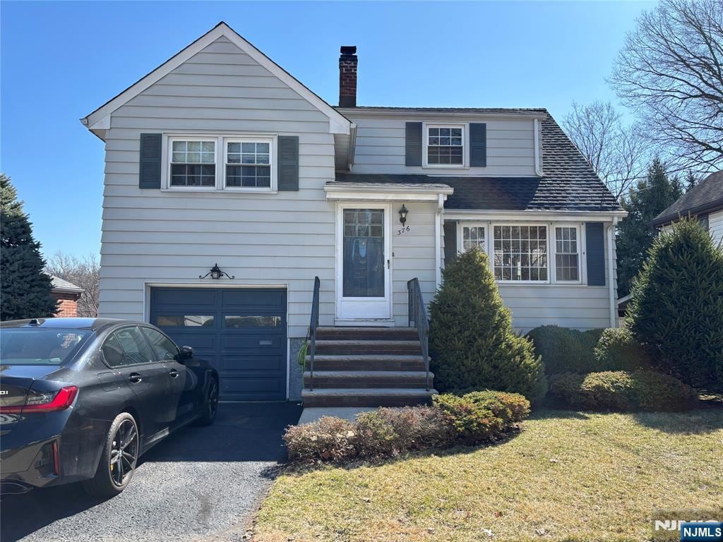 view of front of house featuring an attached garage, a shingled roof, a chimney, a front lawn, and aphalt driveway