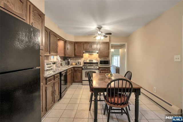 kitchen with light tile patterned floors, backsplash, baseboard heating, under cabinet range hood, and black appliances