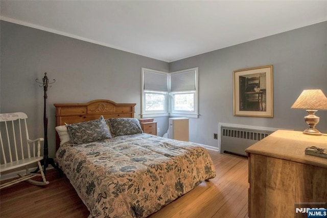 bedroom featuring crown molding, radiator heating unit, wood finished floors, and baseboards